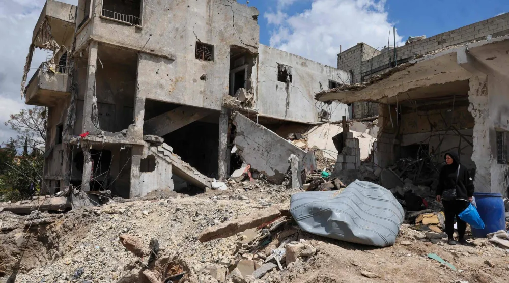 امرأة تحمل بعض المقتنيات الشخصية وسط دمار سببته ضربة إسرائيلية لبلدة كفرصير بجنوب لبنان (أ.ف.ب)