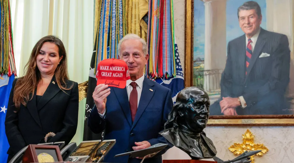 السفير الأميركي في لبنان ميشال عيسى يرفع قبعة كتب عليها «فلنجعل أميركا عظيمة مجدداً» موقعة من الرئيس دونالد ترمب بجوار السفيرة اللبنانية في الولايات المتحدة ندى حمادة معوض في المكتب البيضاوي بالبيت الأبيض - واشنطن العاصمة (رويترز)