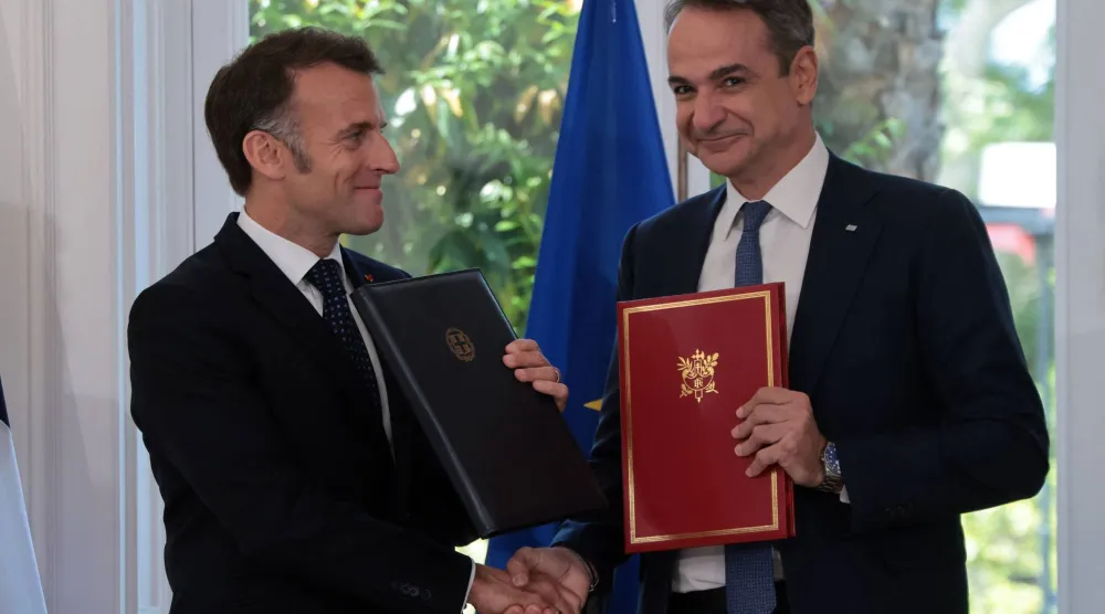 رئيس وزراء اليونان كيرياكوس ميتسوتاكيس يحمل نسخة من الاتفاقات ويصافح الرئيس الفرنسي إيمانويل ماكرون الذي يزور أثينا (أ.ف.ب)