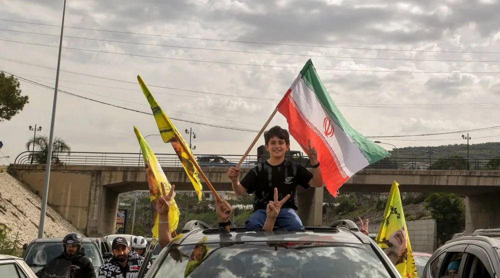 عائلة نازحة في طريق عودتها إلى الجنوب وأطفالها يرفعون أعلام إيران و«حزب الله» (د.ب.أ)