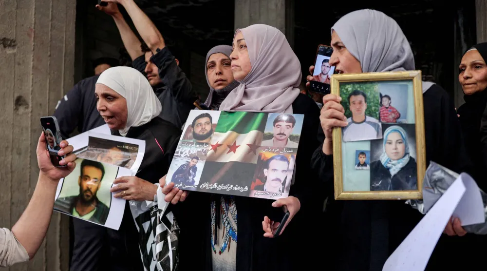 نساء يرفعن صور ضحايا مجزرة التضامن عقب صلاة الجمعة في حي التضامن احتفالاً بتوقيف المتهم أمجد يوسف (رويترز)