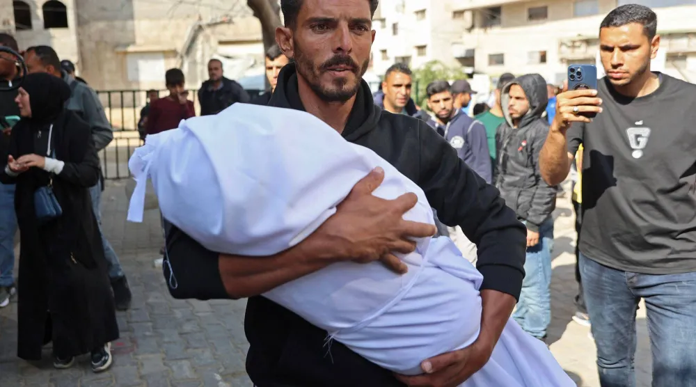 رجل يحمل جثمان طفل أمس السب تقتل جرَّاء قصف مدفعي إسرائيلي على منازل سكنية قرب مستشفى كمال عدوان في بيت لاهيا شمال قطاع غزة (أ.ف.ب)