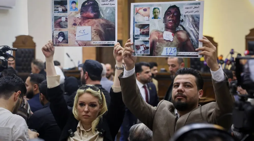 Beşşar Esed döneminde Dera'da Siyasi Güvenlik Şubesi Başkanı olan Atıf Necip'in ilk duruşması sırasında Suriye ayaklanmasının başlarında hayatını kaybeden çocukların fotoğraflarını kaldıran aktivistler (AP)