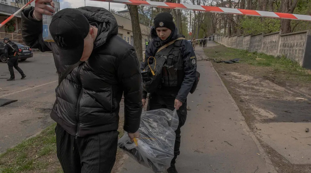 شرطي أوكراني (يمين) ويساعده رجل آخر يحملان كيساً بلاستيكياً يحتوي على حطام طائرة مسيّرة بموقع غارة روسية بطائرة مسيّرة في كييف 28 أبريل 2026 (أ.ف.ب)