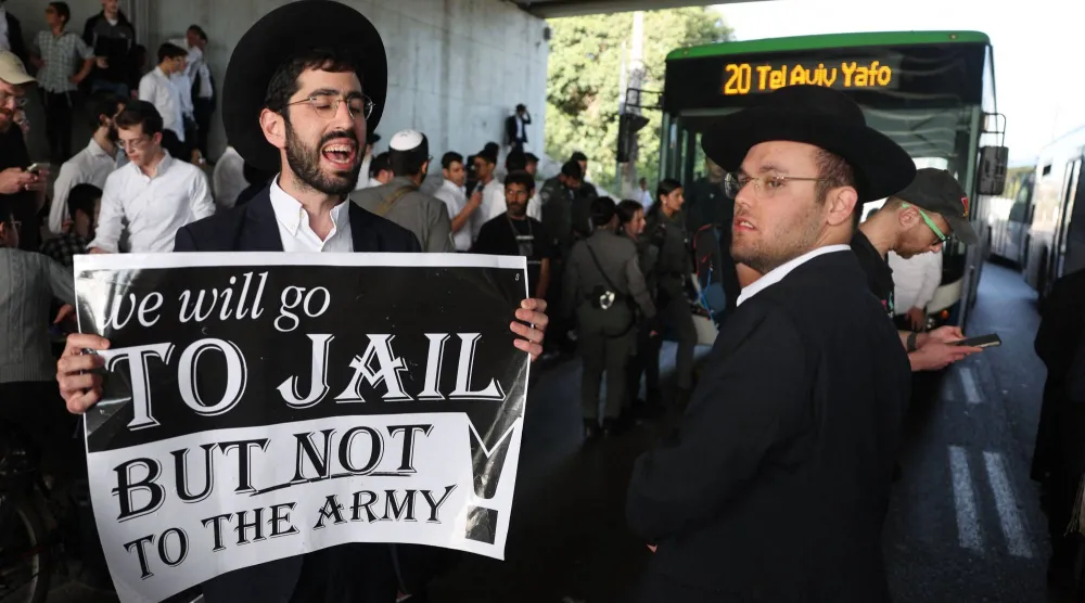  محتج من اليهود المتشددين الرافضين للتجنيد يحمل لافتة أثناء احتجاجه مع آخرين ضد التجنيد الإجباري (ا.ف.ب)