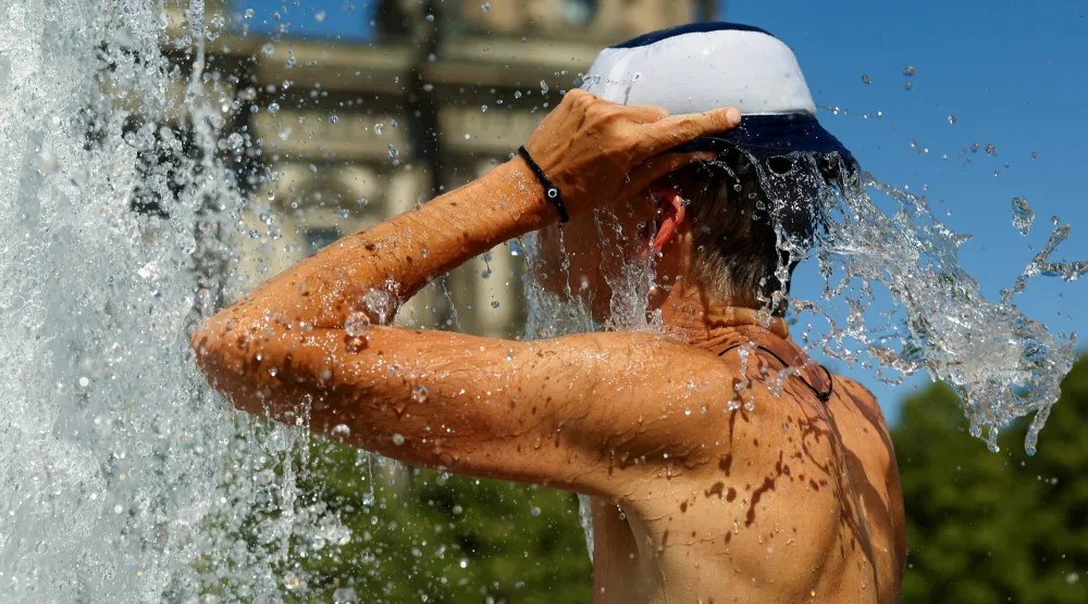 رجل يبرِّد نفسه في نافورة أمام كاتدرائية برلين خلال يوم صيفي حار (رويترز)