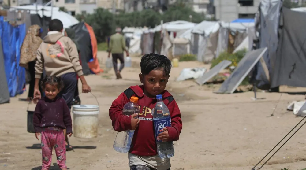 أطفال يجلبون مياه الشرب في مخيم بريج للاجئين الفلسطينيين وسط قطاع غزة (أ.ف.ب)