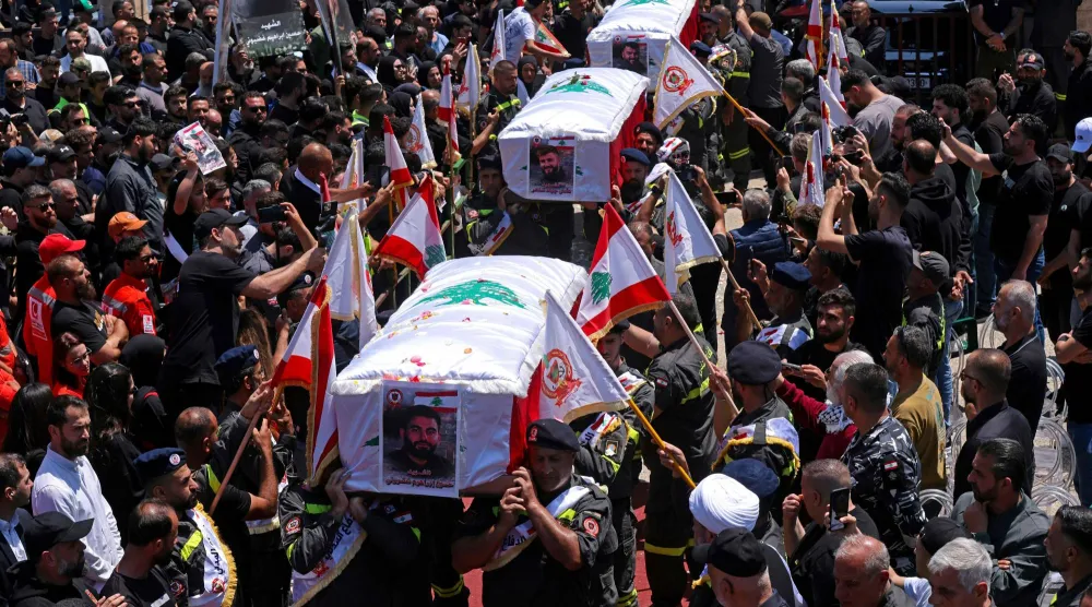 يحمل المشيعون نعوش ثلاثة من عناصر الدفاع المدني اللبناني الذين استشهدوا في غارة جوية إسرائيلية على بلدة مجدل زون خلال جنازتهم في مدينة صور الجنوبية (رويترز)