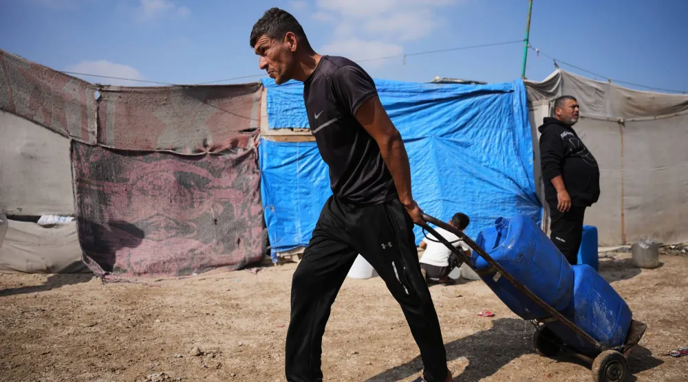 فلسطيني يحمل عبوات ماء مملوءة بين خيام النازحين في مدينة خان يونس جنوب قطاع غزة يوم الخميس (أ.ب)