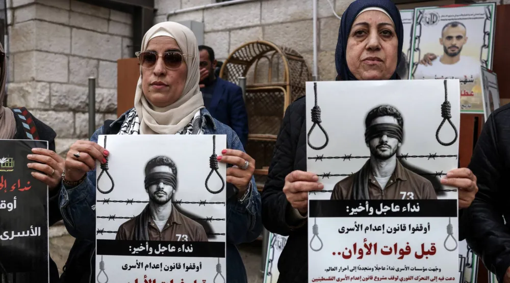 Protesters hold placards outside the Red Cross offices in Ramallah, in the Israeli-occupied West Bank, on March 31, 2026, during a rally against a bill approved by Israel's parliament that would allow the execution of Palestinians convicted on terror charges for deadly attacks. (AFP via Getty Images) 