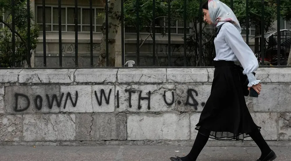 A woman walks past an anti-US graffiti painted on the wall of the Tehran University on Enqelab-e-Eslami street in downtown Tehran, Iran, Saturday, April 25, 2026. (AP)