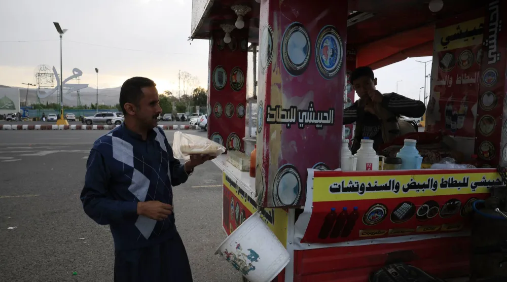 شخص يشتري وجبات خفيفة من عربة متنقلة في صنعاء الخاضعة للحوثيين (إ.ب.أ)