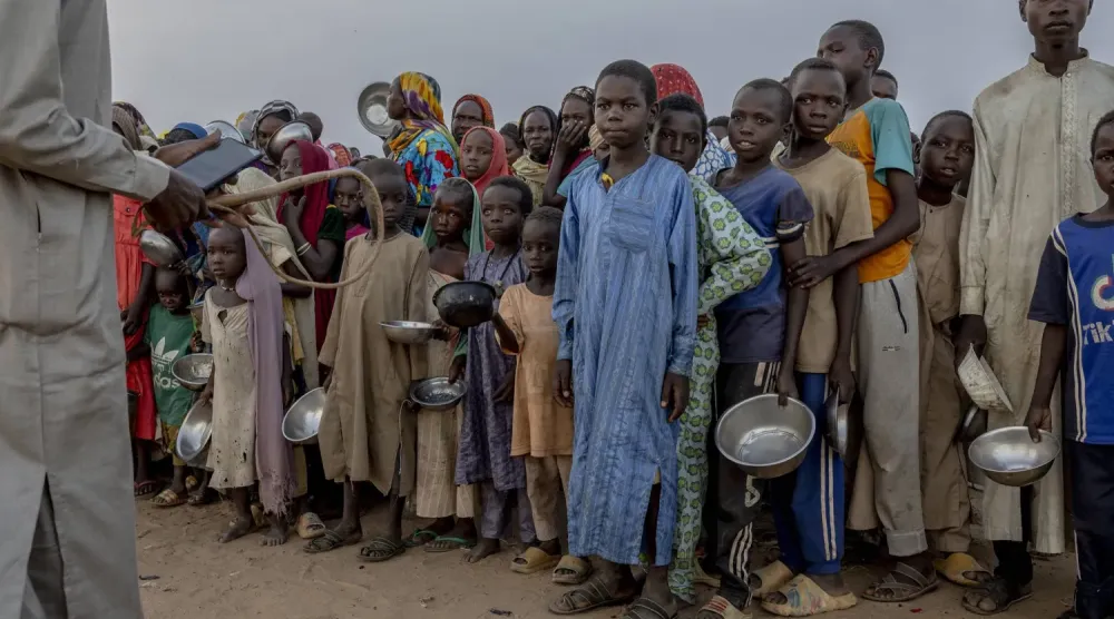 Sudan-Çad sınırında yer alan Adré (Adri) Mülteci Kampı’nda bir grup Sudanlı mülteci çocuk yemek almak için itişip kakışırken, elinde kırbaç tutan bir adam onları kontrol altına almaya çalışıyor (NYT)