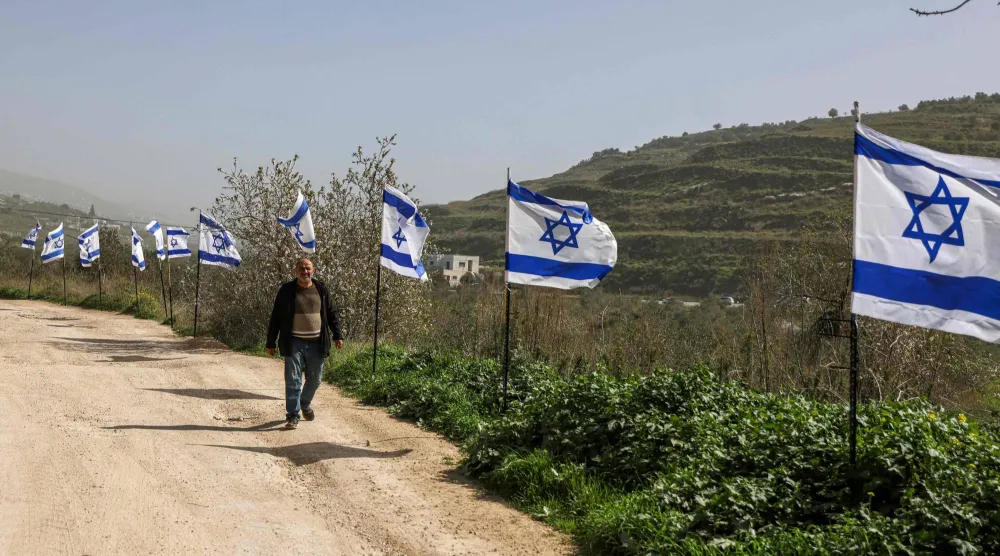 فلسطيني يمرّ بجوار سياج من الأعلام الإسرائيلية نصبه مستوطنون بعد استيلائهم على محطة قطار تعود إلى العصر العثماني في قرية برقة شمال الضفة فبراير الماضي (أ.ف.ب)