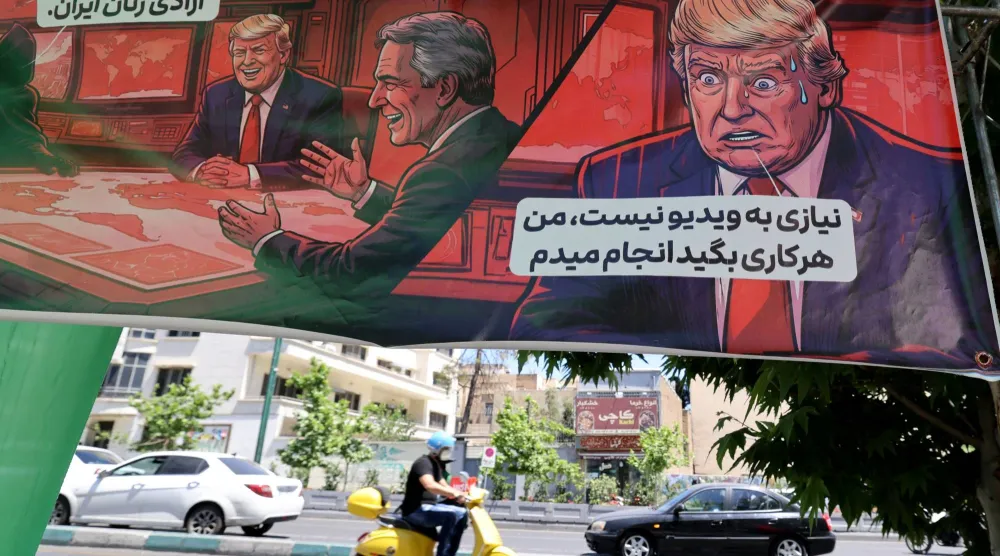 إيراني يقود دراجة نارية أمام لافتة تعرض رسماً للرئيس الأميركي وتضم عبارتين: «إذن نحن ذاهبون من أجل حرية النساء الإيرانيات» (يسار) و«لا حاجة إلى فيديو.. سأفعل كل ما تقول» (يمين) في طهران يوم 9 مايو 2026 (أ.ف.ب)