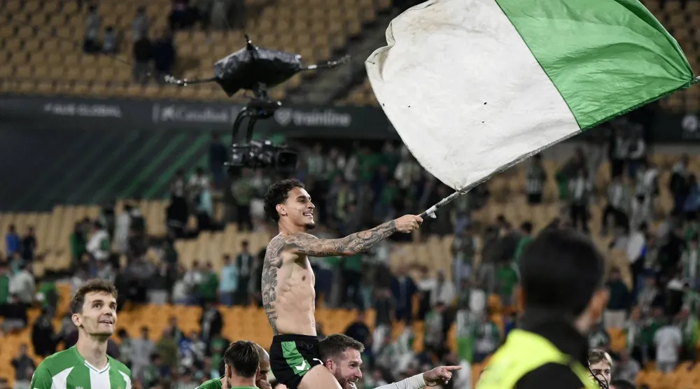 البرازيلي أنتوني نجم ريال بيتيس يلوّح بعلم الفريق احتفالاً بالتأهل لدوري الأبطال (أ.ف.ب)