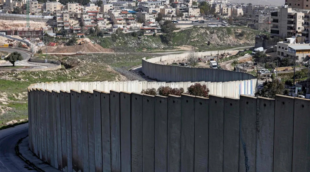 صورة لمستوطنة بسغات زئيف الإسرائيلية (يسار) التي بنيت في ضاحية من ضواحي القدس الشرقية ذات الأغلبية العربية خلف جدار الفصل الإسرائيلي في 16 فبراير الماضي (أ.ف.ب)