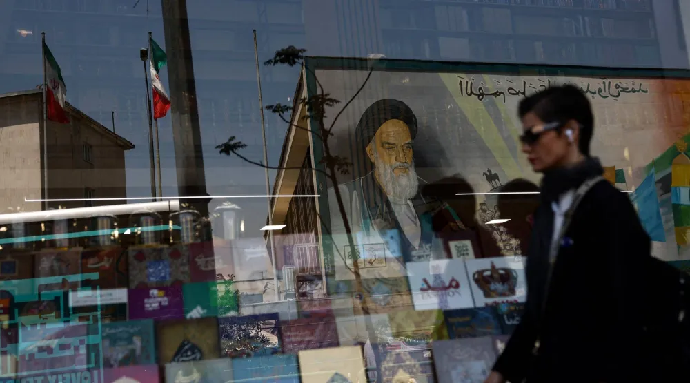 إيرانية تمر أمام جدارية للمرشد الأول(الخميني) تنعكس على واجهة مكتبة في طهران (رويترز)