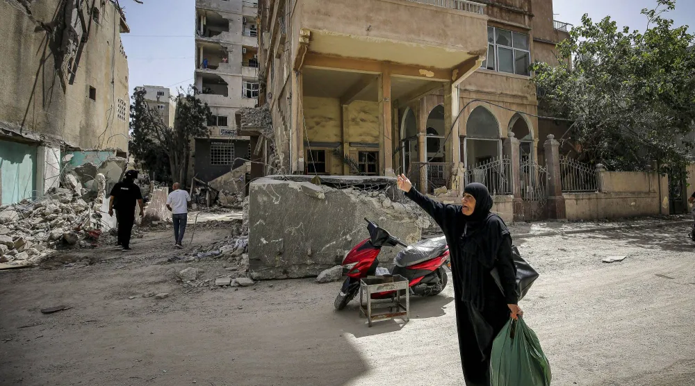 سيدة لبنانية مسنة في أحد شوارع مدينة صور وخلفها يظهر مبنى متضرر جراء الغارات الإسرائيلية (د.ب.أ)