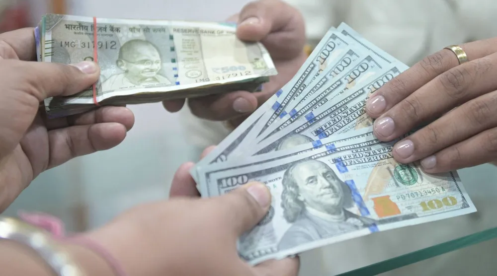 أشخاص يحملون أوراقاً نقدية من الدولار والروبية الهندية (أ.ف.ب)