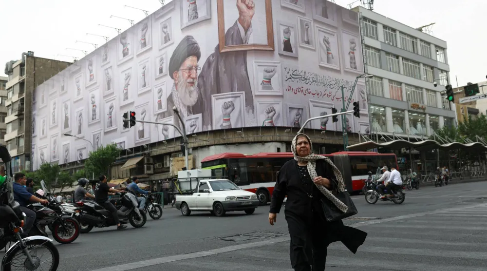 سيدة تسير في أحد شوارع طهران وفي الخلفية لافتة عملاقة تحمل صورة المرشد السابق علي خامنئي (رويترز)