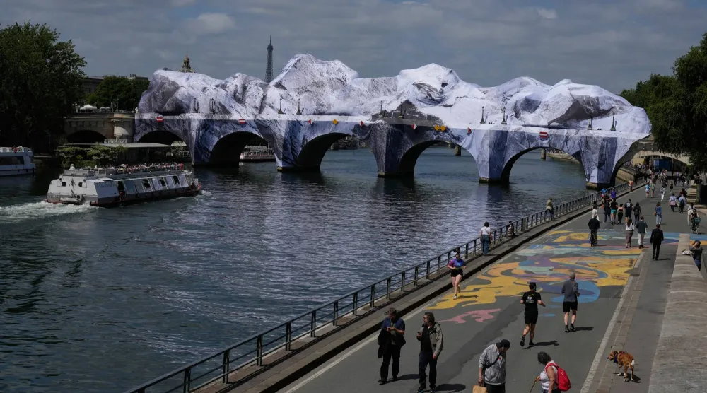 People walk along the Seine river next to "The Pont Neuf Cave," an inflated art installation by French street artist JR, on Paris' oldest bridge, the Pont Neuf, Thursday, May 21, 2026, which will be open to the public from June 6-28. (AP Photo/Michel Euler)