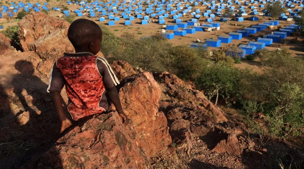 Kasım 2023’te Sudan-Çad sınırı yakınındaki mülteci kampına bakan bir tepenin üzerinde oturan çocuk. (Reuters)