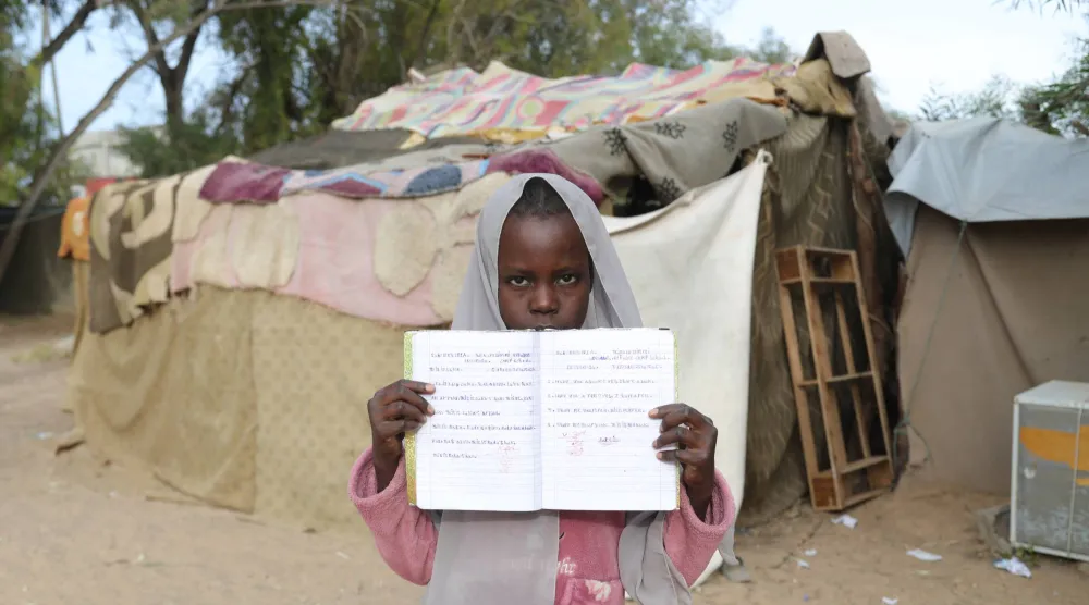 تلميذة سودانية ترفع كراستها أمام فصلها في مدرسة للاجئين في تاجوراء شرق العاصمة الليبية طرابلس يوم 18 مايو 2026 (أ.ب)