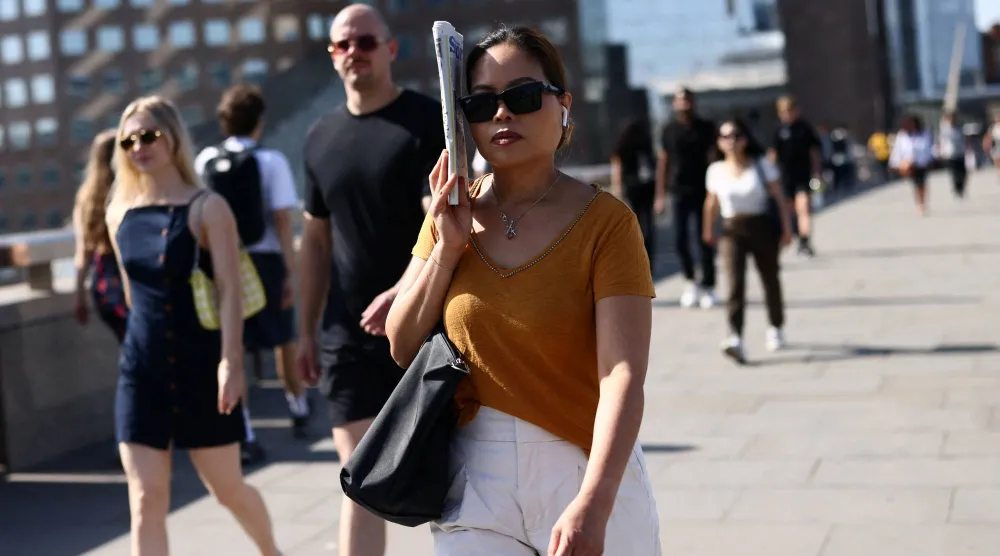 A woman shields herself from the sun with a newspaper as she crosses London Bridge during a heatwave in London, Britain, May 26, 2026. REUTERS/Jack Taylor