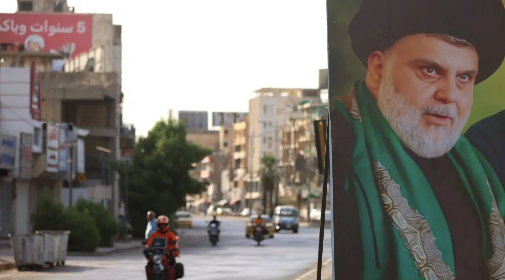 دراجة نارية تمر أمام لافتة لمقتدى الصدر نُصبت على أحد شوارع بغداد 27 مايو 2026 (أ.ف.ب)