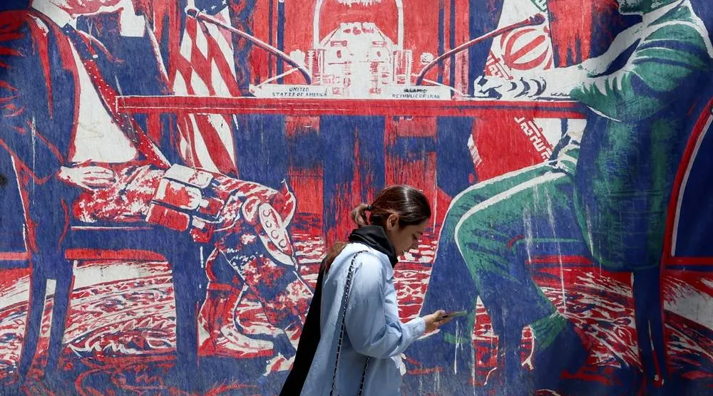 An Iranian girl walks next to an anti-US mural depicting Iran and US negotiations at a table, near the former US Embassy in Tehran, Iran, 26 May 2026. (EPA)