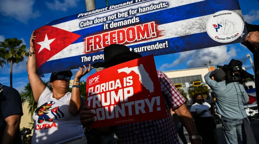 Miami'deki Versailles restoranının önünde, ABD'nin eski Küba Devlet Başkanı Raúl Castro'ya yönelttiği suçlamaları destekleyen pankartlar taşıyan insanlar, 20 Mayıs 2026 (AFP)