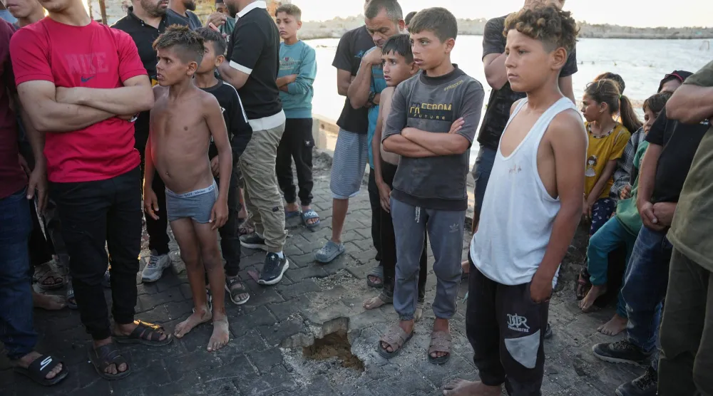 فلسطينيون يقفون قرب موقع سقوط شظايا غارة إسرائيلية في ميناء مدينة غزة يوم الأحد (أ.ب)