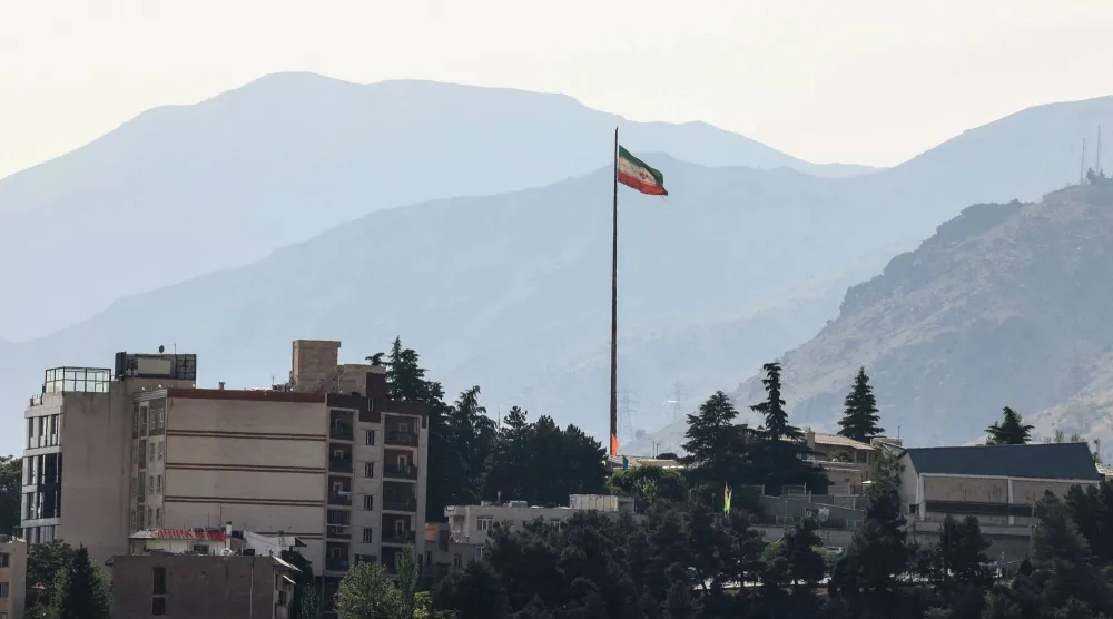 The Iran flag flutters from a tall flagpole over high-rise buildings in northern Tehran on May 12, 2026. (AFP)