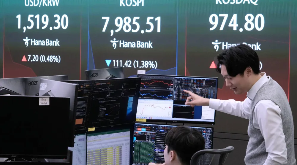 متداولان في بنك هانا وبجانبهما شاشة تعرض مؤشر «كوسبي» وسعر صرف الدولار والوون الكوري الجنوبي (أ.ب)