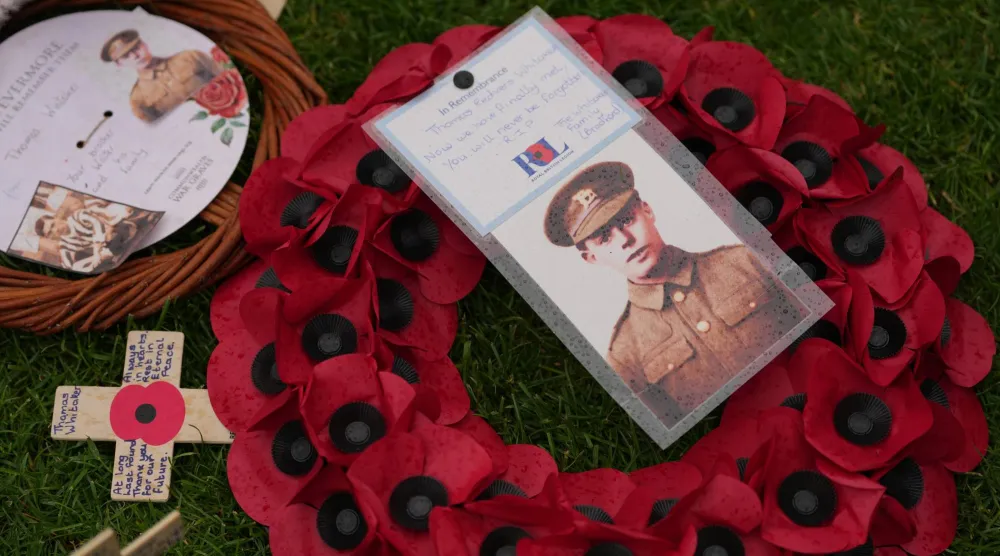 A poppy wreath and a photo next to the grave of Private Thomas Redvers Whitaker during a burial ceremony for six British soldiers of World War I, at the CWGC's Tyne Cot Cemetery in Zonnebeke, Belgium, Wednesday, June 10, 2026. (AP Photo/Virginia Mayo)