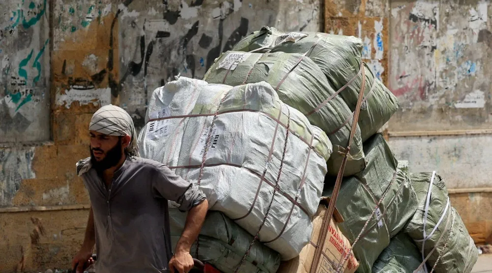 عامل يسحب عربة محملة بالبضائع لتوصيلها إلى سوق قريبة في كراتشي بباكستان (رويترز)