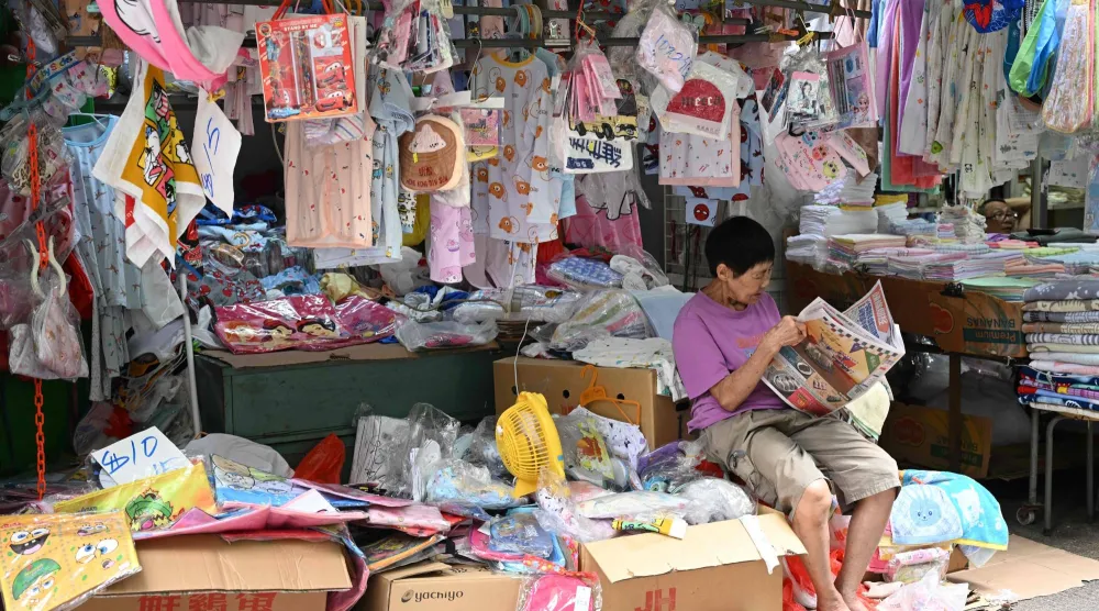 سيدة تقرأ صحيفة أمام متجرها في مدينة هونغ كونغ (أ.ف.ب)