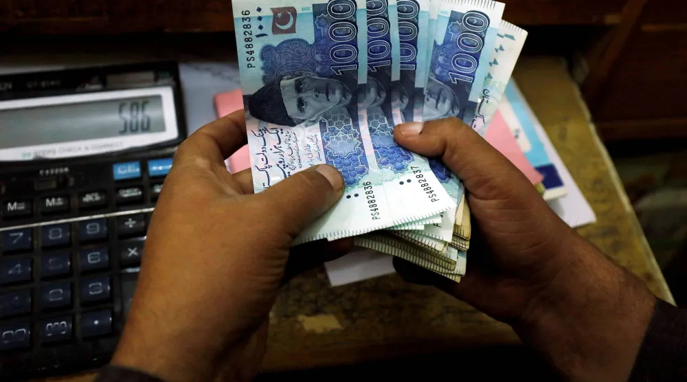 متداول يعدّ أوراقاً نقدية من الروبية الباكستانية داخل أحد أكشاك صرافة العملات في مدينة بيشاور (رويترز)