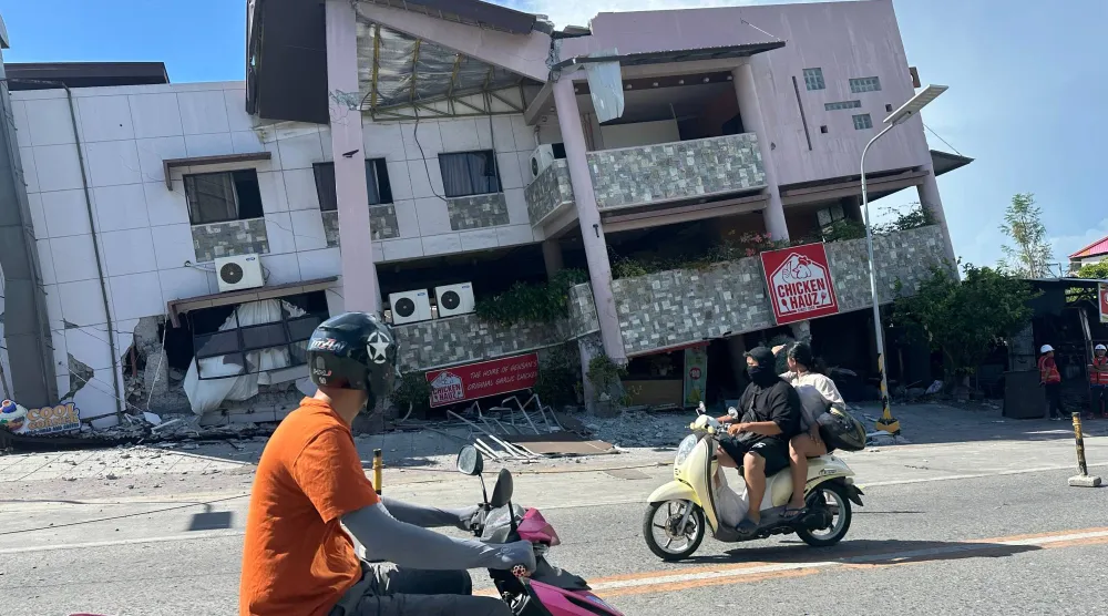 السكان يمرون بجوار مبنى منهار بعد زلزال ضرب مدينة جنرال سانتوس في الفلبين (أ.ب)