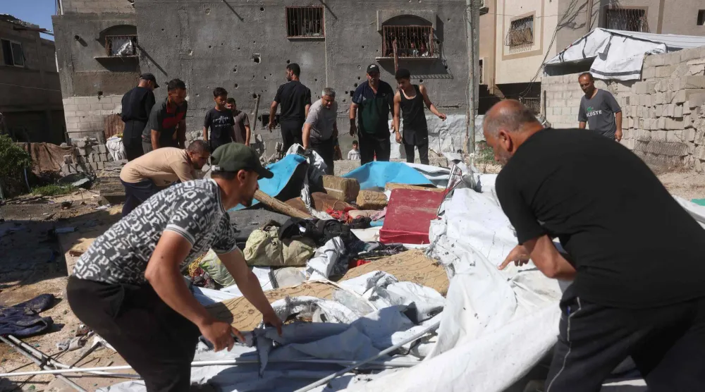 نازحون فلسطينيون يزيلون الرمال والحطام عقب غارة عسكرية إسرائيلية استهدفت خيامهم (أ.ف.ب)