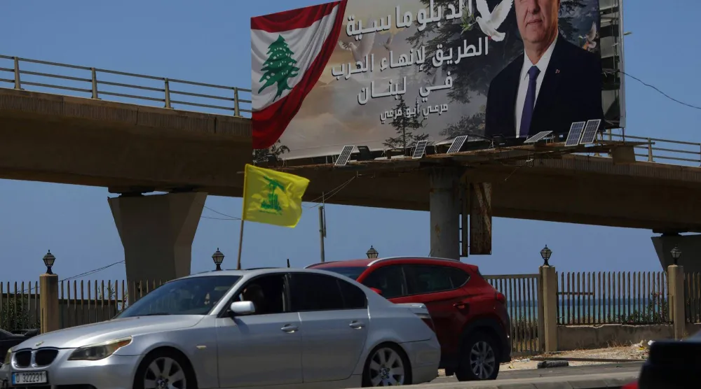 سيارة ترفع علم «حزب الله» في مدينة صيدا وبدت لوحة إعلانية للرئيس اللبناني جوزيف عون كُتب عليها: «الدبلوماسية هي السبيل لإنهاء الحرب في لبنان» (أ.ف.ب)