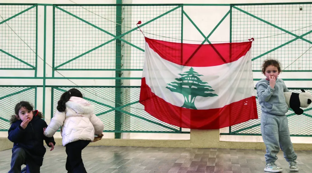 أطفال نازحون يلعبون في مدرسة تحولت إلى مركز للنزوح ومن خلفهم العلم اللبناني (رويترز)