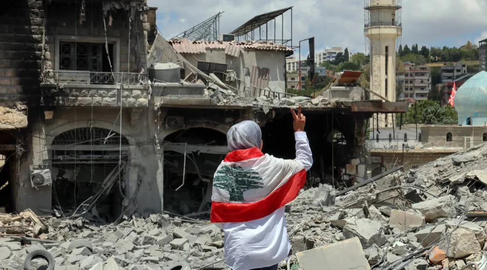لبنانية تضع العَلَم اللبناني على كتفيها وتتفقد الدمار في ساحة مدينة النبطية بجنوب لبنان (إ.ب.أ)