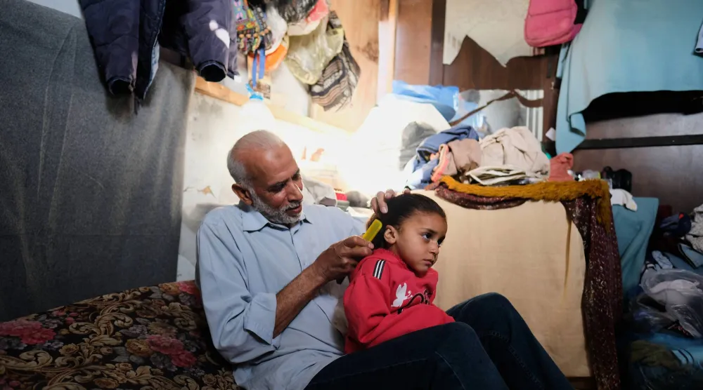 الفلسطيني محمود نوفل يمشط شعر حفيدته رنين (3 سنوات) والتي يتولى رعايتها مقتل والديها في غارة إسرائيلية على خان يونس (أ.ب)
