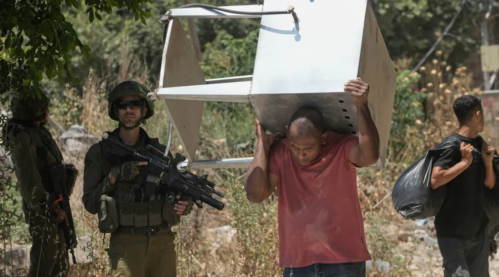 فلسطيني يحمل أغراضه من مخيم طولكرم بالضفة الغربية المحتلة بعدما منح الجيش الإسرائيلي بعض السكان تصريحاً لفترة قصيرة لجمع متعلقاتهم من المنازل التي أجبرهم على النزوح عنها (أ.ب)
