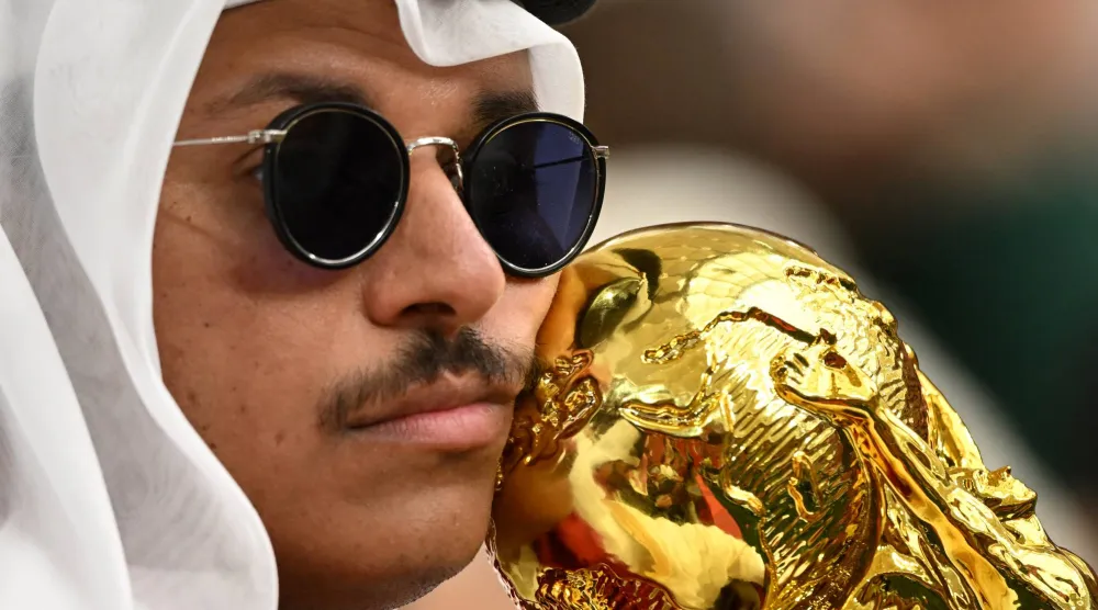 مشجع قطري ممسكاً بمجسم لكأس العالم في المدرجات (رويترز)
