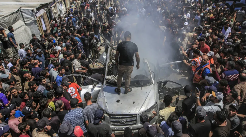 فلسطينيون يتفقدون مركبة مدمرة عقب غارة جوية إسرائيلية على مدينة غزة (إ.ب.أ)