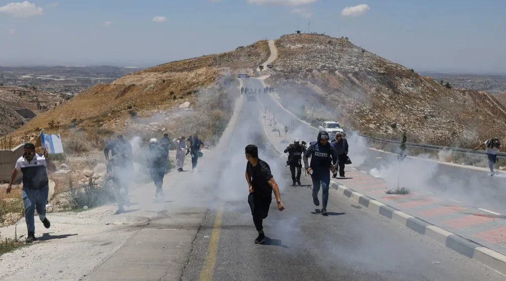 فلسطينيون بينهم ملاك أراضٍ يفرون من الغاز المسيل الذي أطلقته قوات إسرائيلية بينما كانوا يحتجون على مصادرة أملاكهم لصالح مستوطنة قرب بلدة دورا في الضفة الغربية المحتلة يوم الجمعة الماضي (أ.ف.ب)
