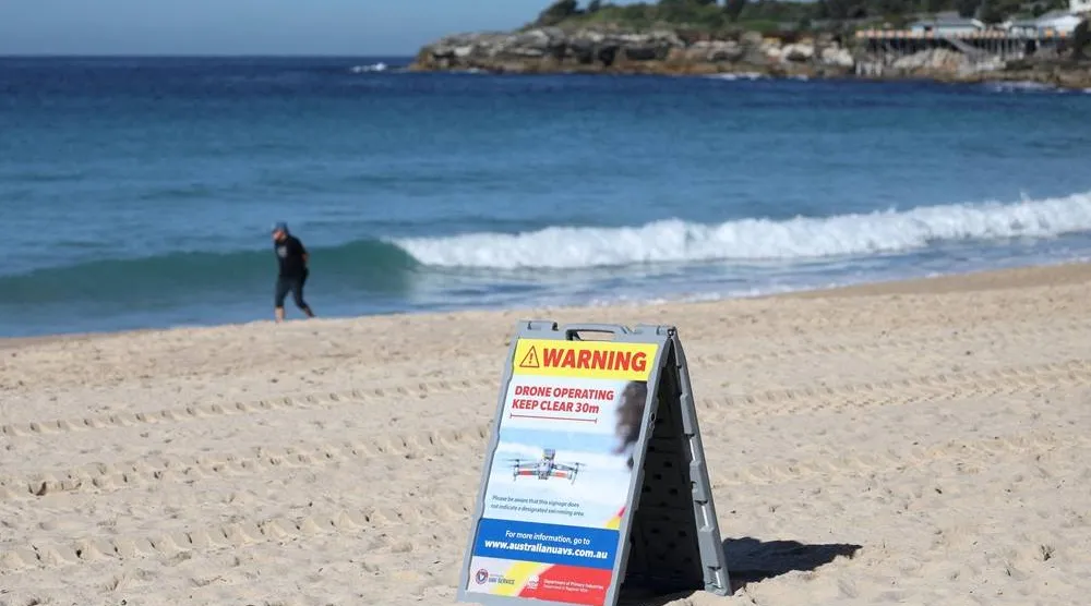 A warning sign notifying the public that a shark-spotting drone is operating in the area is displayed at Coogee Beach following a shark attack on Saturday, in Sydney, Australia, June 16, 2026. (Reuters)